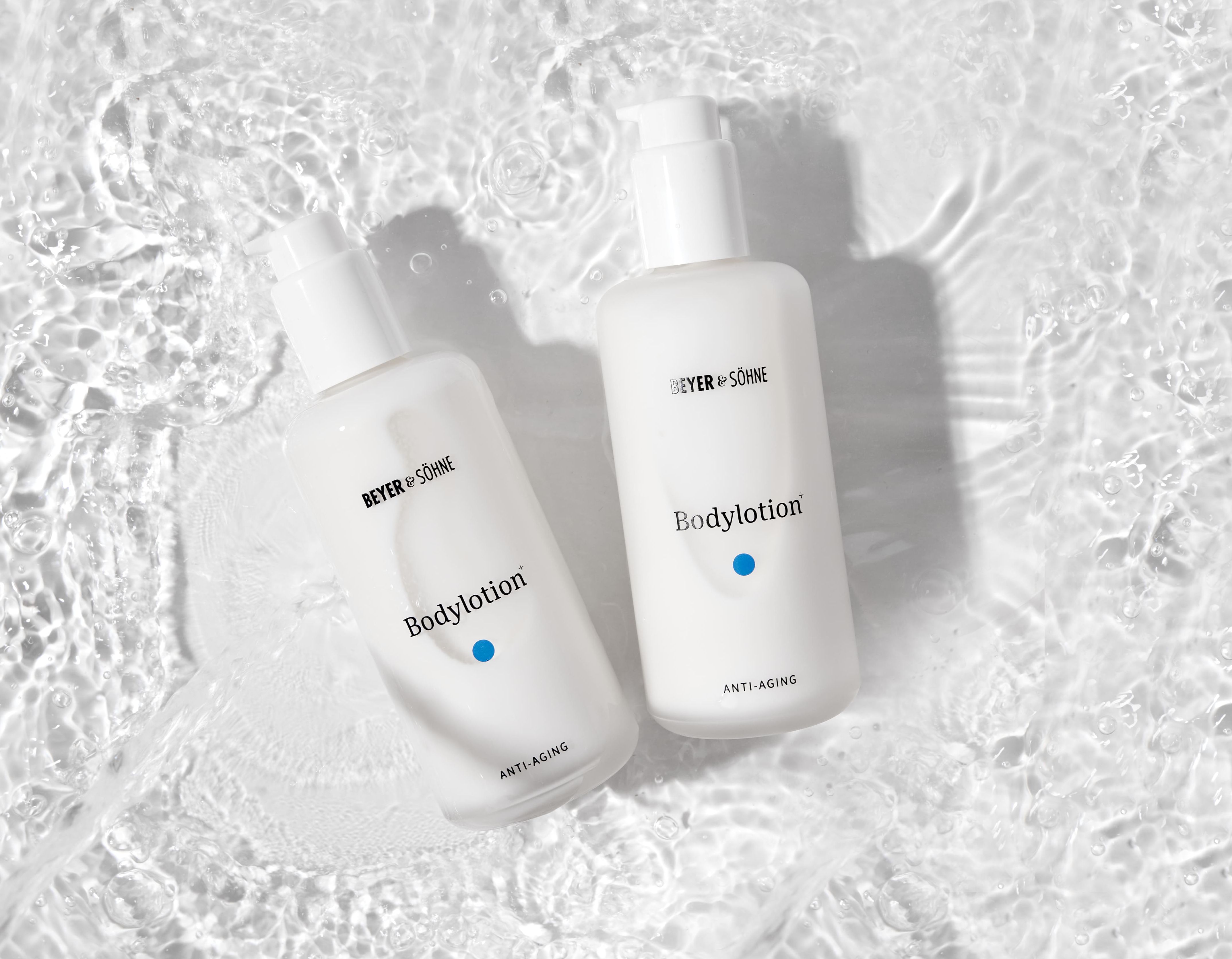 Weiße Flaschen der Beyer & Söhne Bodylotion Anti-Aging auf sprudelnder Wasseroberfläche - reichhaltige Pflege für trockene und empfindliche Haut.
